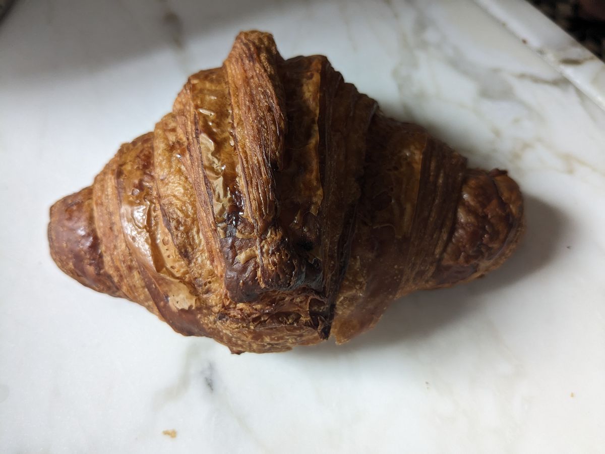 A very dark croissant on a white marble background.