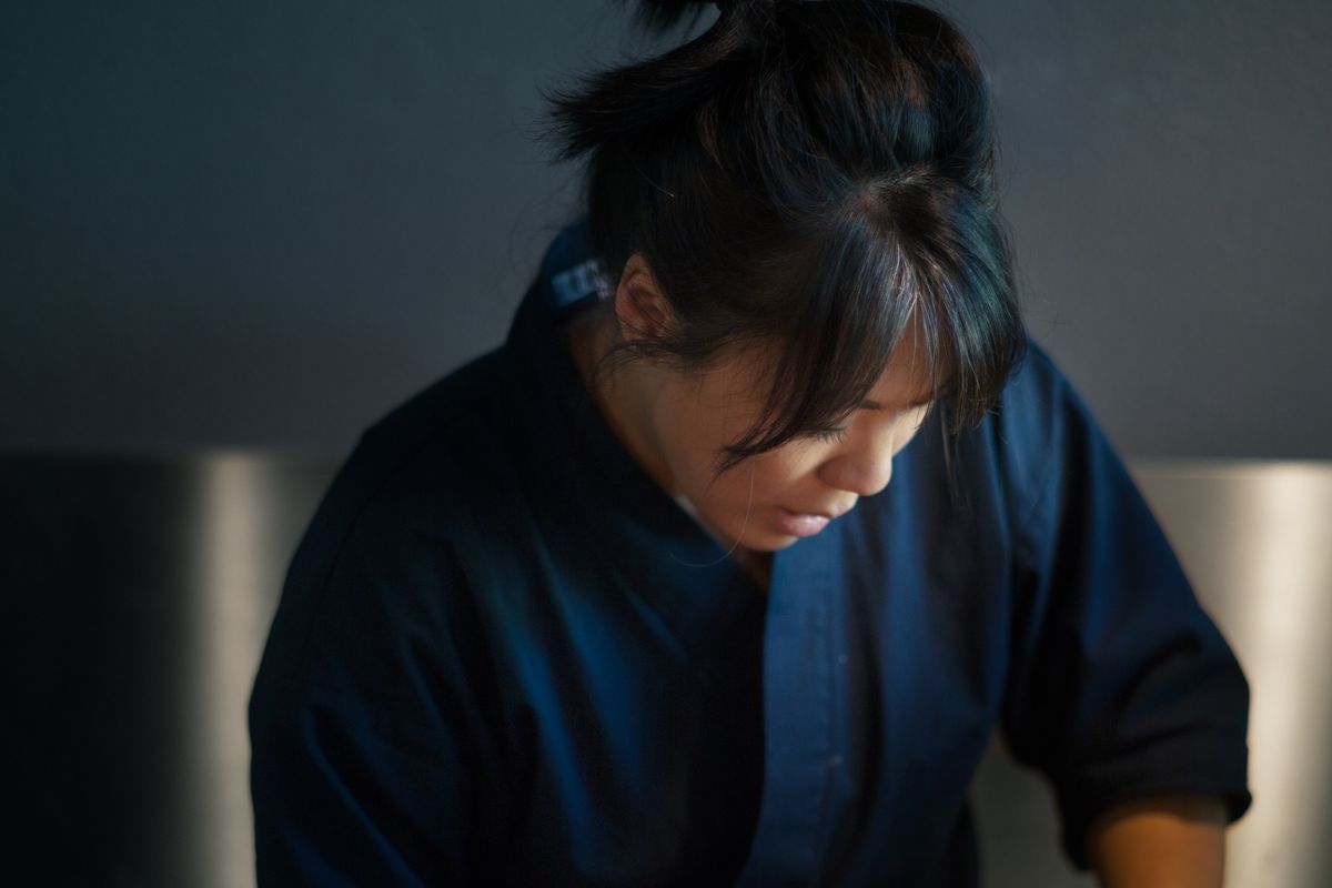 A Korean-American woman wearing a blue chef’s jacket, her hair in a ponytail, scoops rice at the counter of Zilla Sake