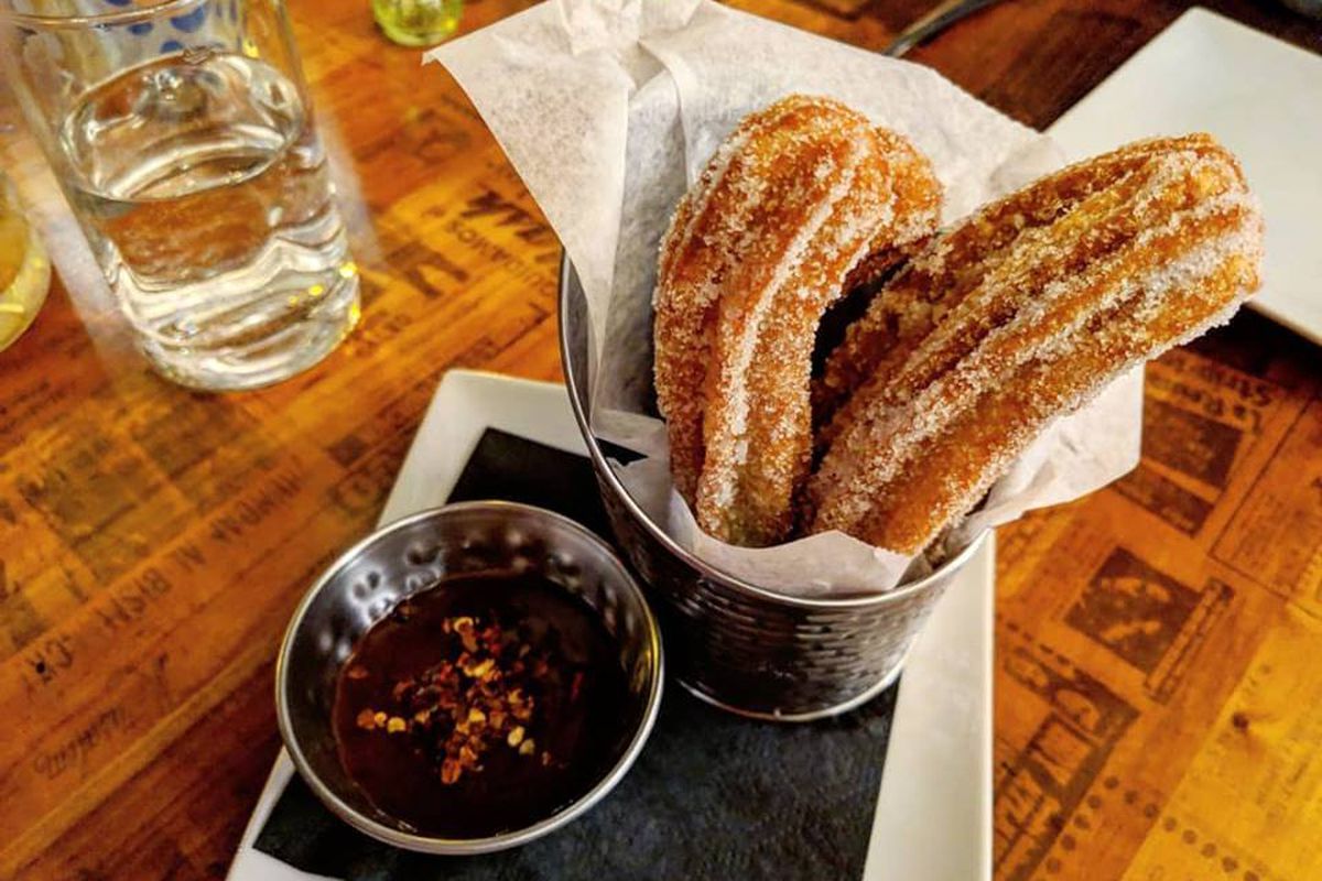 Churros stick out of a metal pail lined with paper, alongside a spicy chocolate dipping sauce, at Gustazo in Cambridge