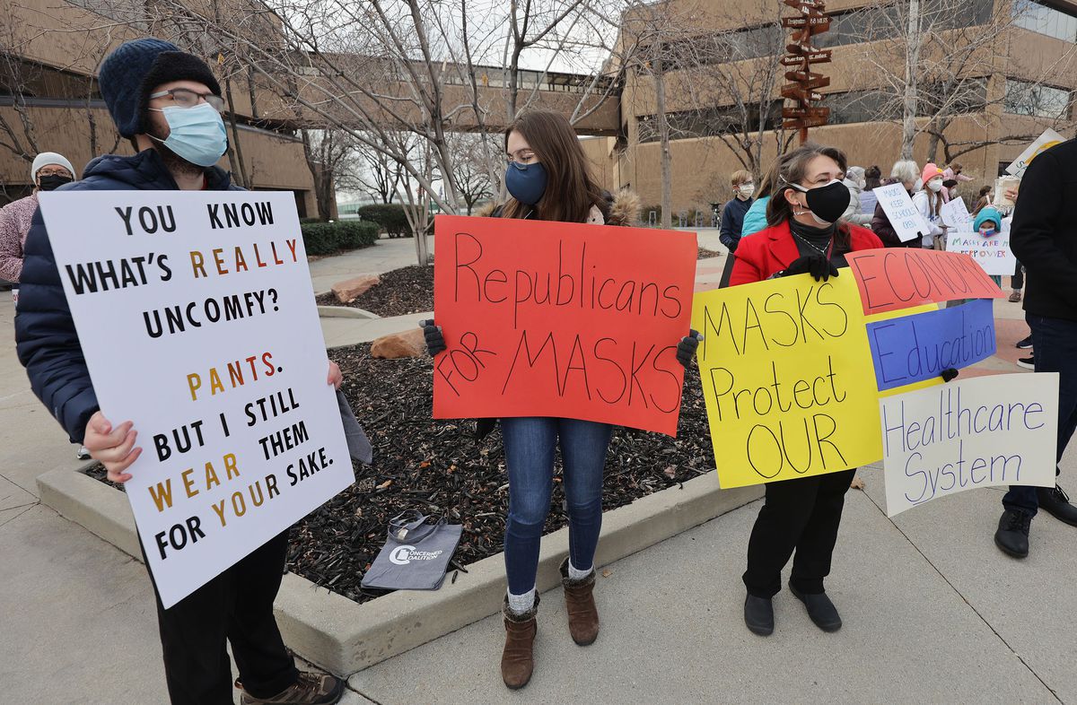 Ian Wagman, Suzannah Rose and Francesca Rose hold signs as the Salt Lake County Council votes in Salt Lake City on Thursday, Jan. 13, 2022.&nbsp;The council voted to leave a 30-day county mask order in place.