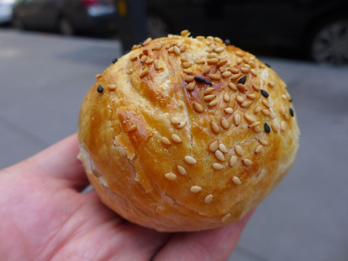 A round turnover topped with seeds is held in a hand.