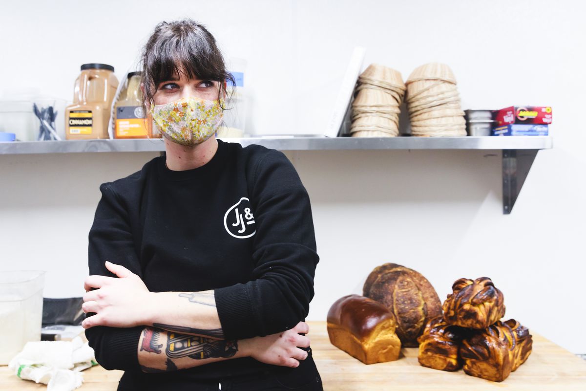 A woman in a black sweatshirt and a floral fabric face mask stands in front of a restaurant prep counter.