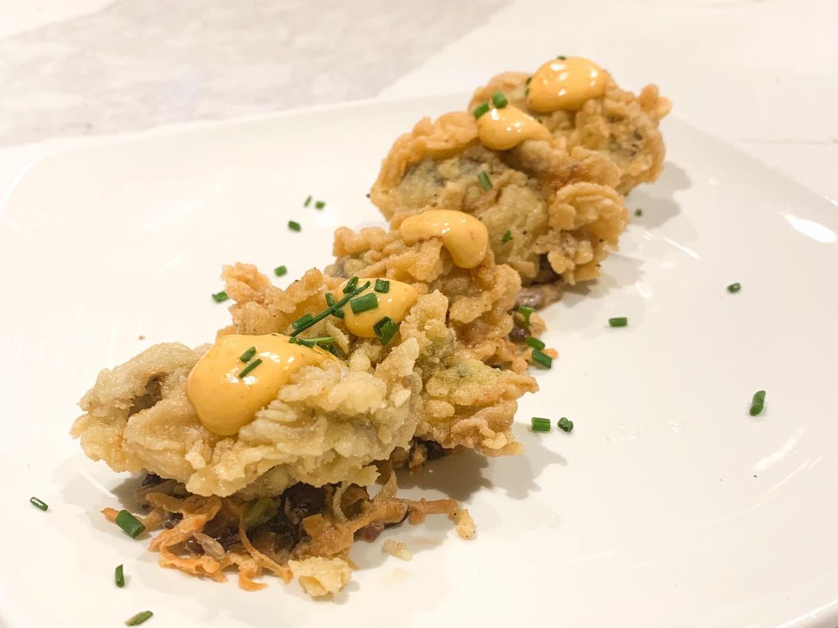 A line of fried oysters with a dollop of orange sauce and green chives sprinkled on top of each one.