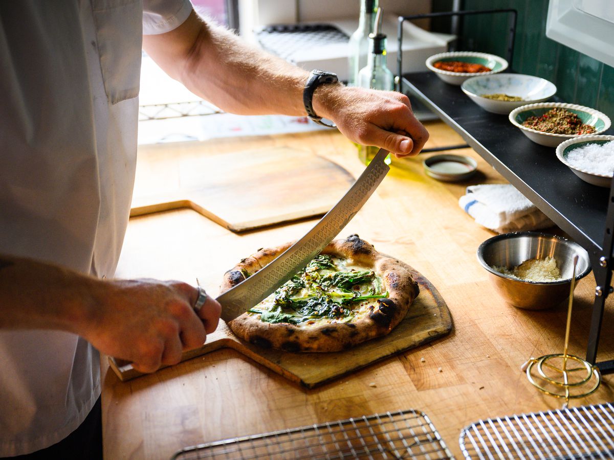 Craig Melillo cuts a pizza with crescendo cheese, asparagus, spinach, green garlic and mozzarella at Gracie’s Apizza.