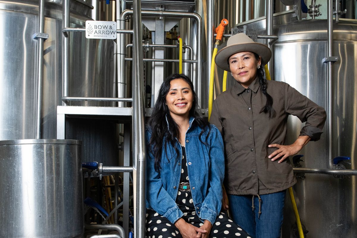Two women pose in front of brewery tanks