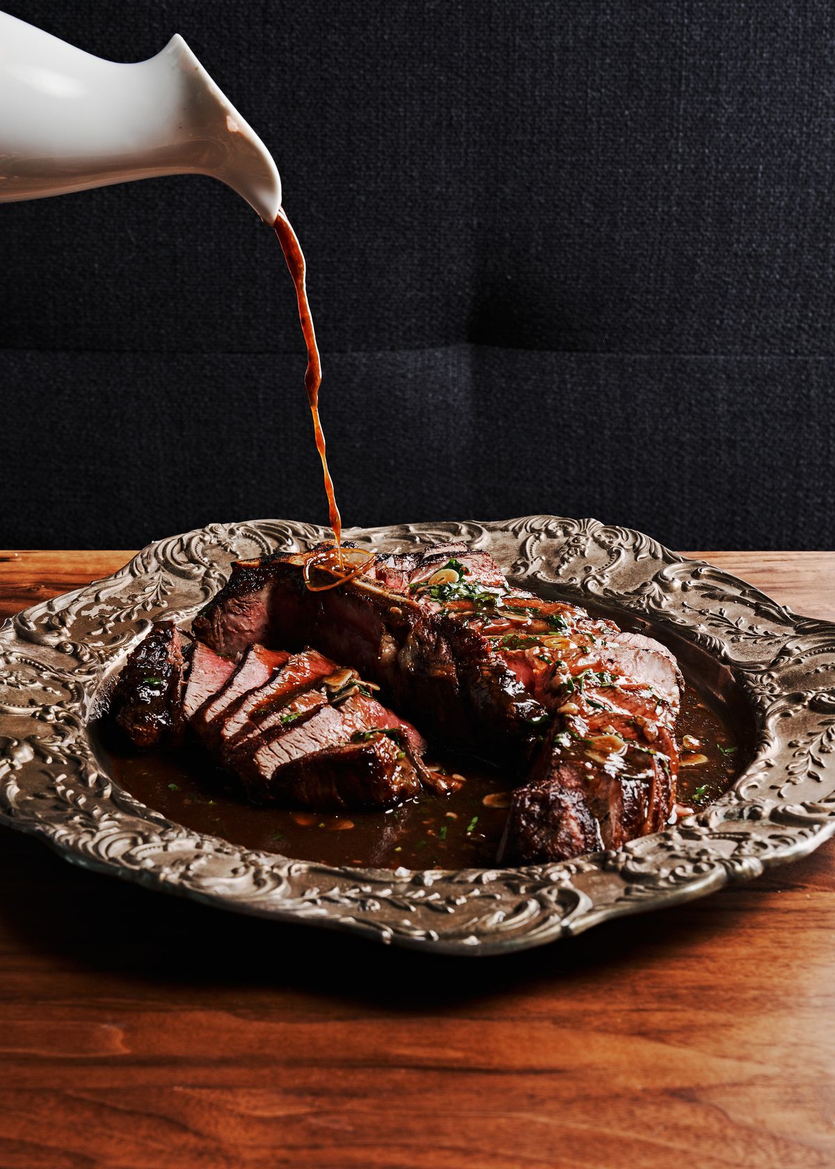A silver platter with a sliced porterhouse steak topped with herbs and sauce