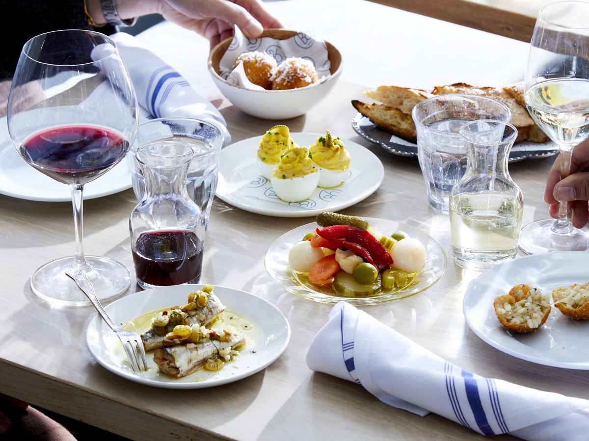 Wine glasses and small plates filled with food scattered on a white tabletop.