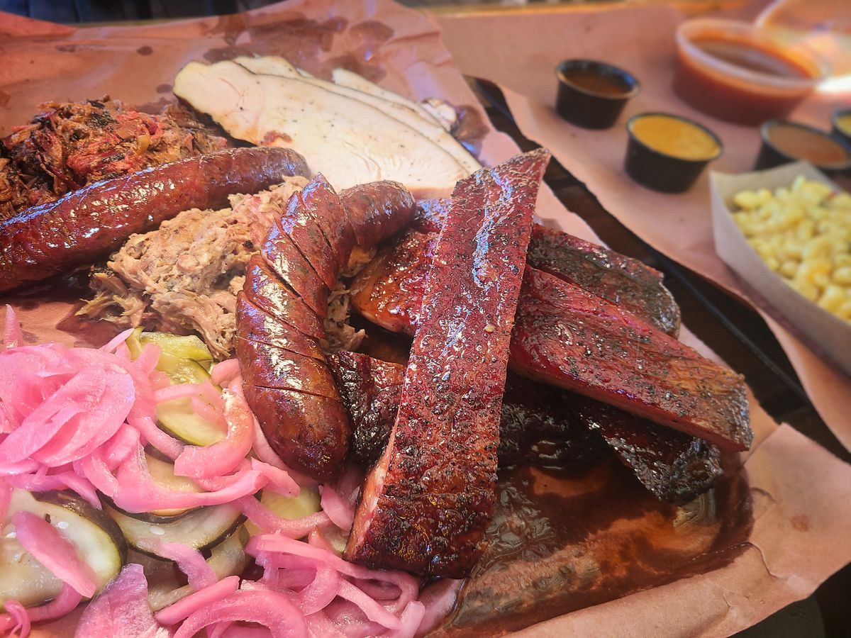 Smoked ribs, pulled pork, and smoked turkey breast are shown on a platter, atop a wooden table.