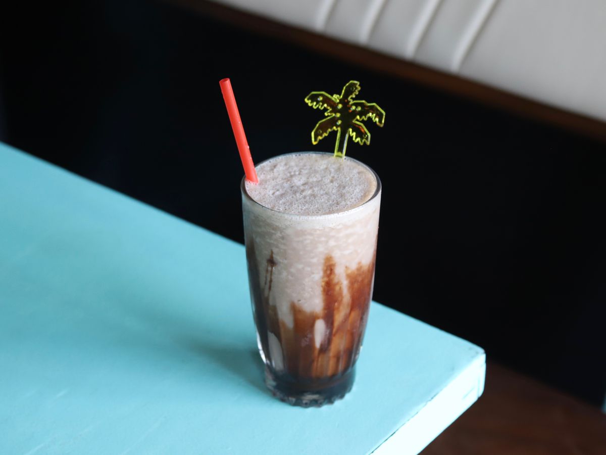 A frozen mudslide cocktail sits on a turquoise table. It’s garnished with a small plastic palm tree.