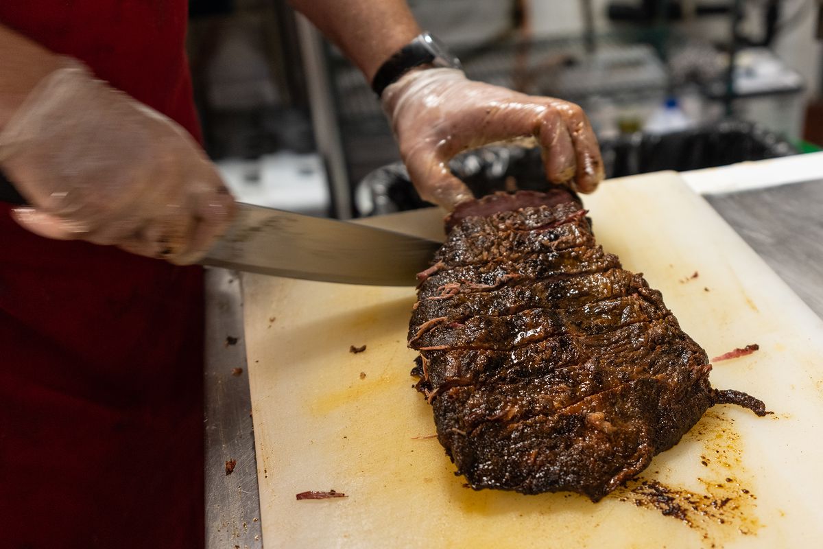 A cook slices brisket on a cutting board. 