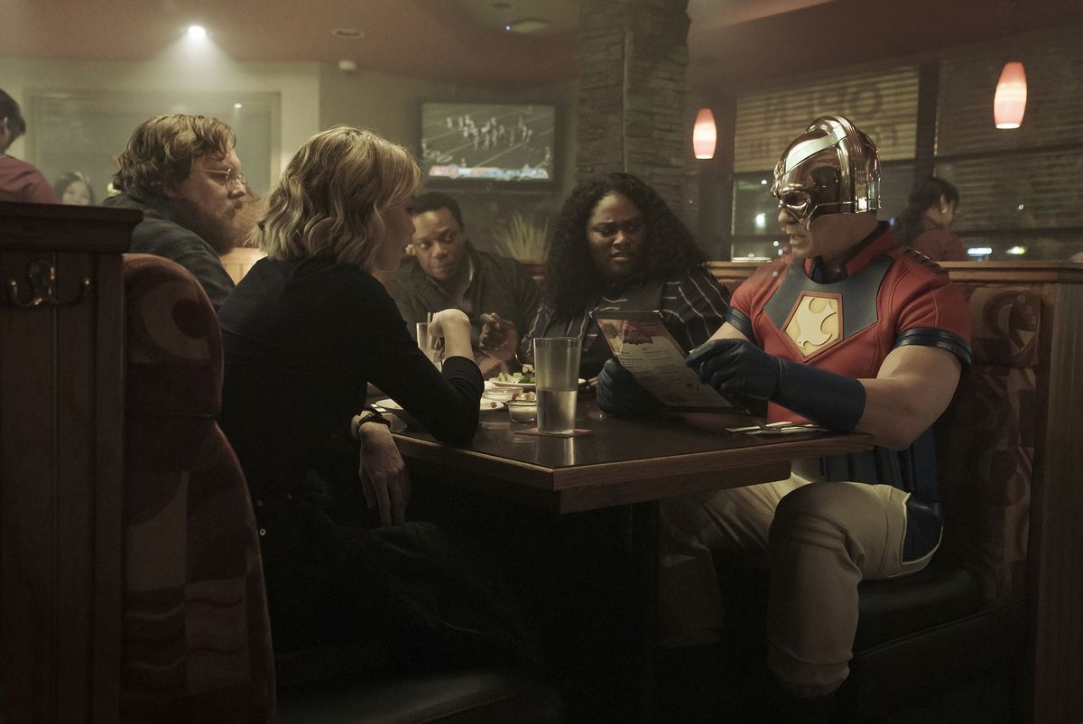 The whole team of Peacemaker sitting in a booth at a family restaurant in a still from episode 1