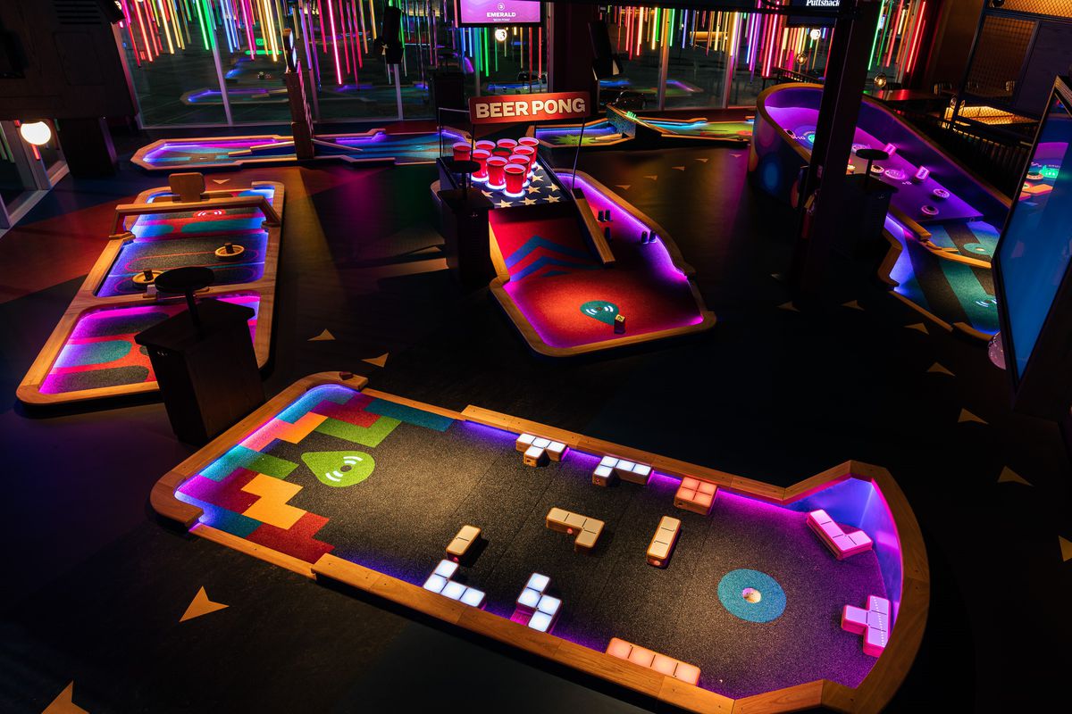 Four neon-lit indoor miniature golf greens with a beer pong sign in the background