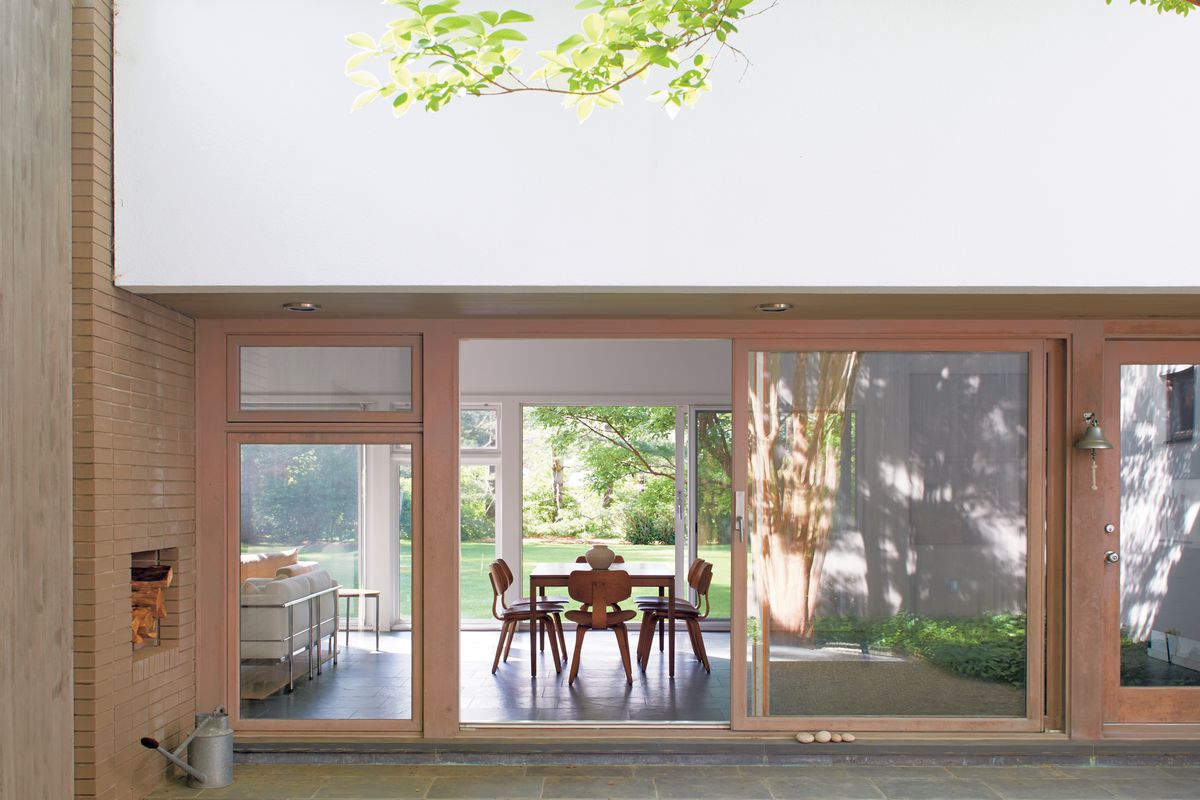 Exterior shot looking into a simple dining room with glazed walls on two sides and a yard seen on the other side. 