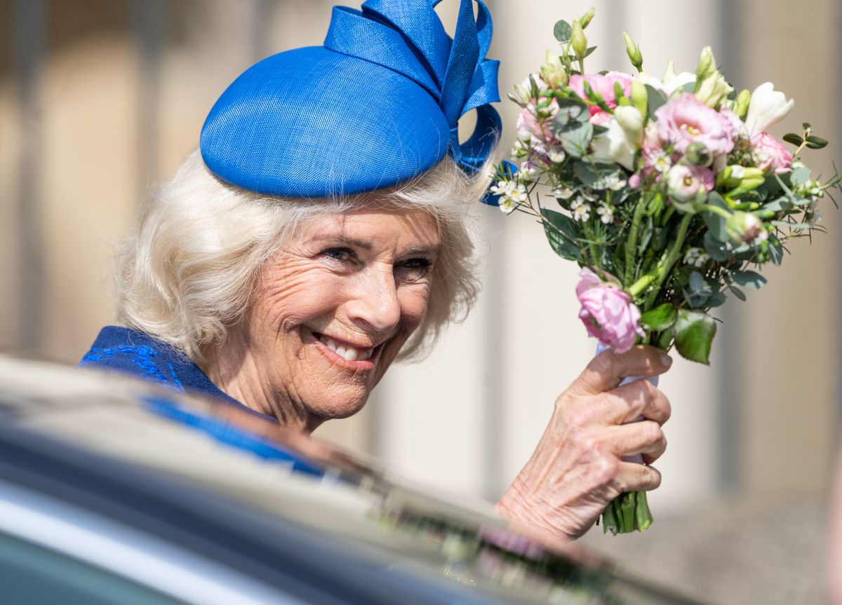 Camilla wears a blue fascinator and holds up a bouquet. 