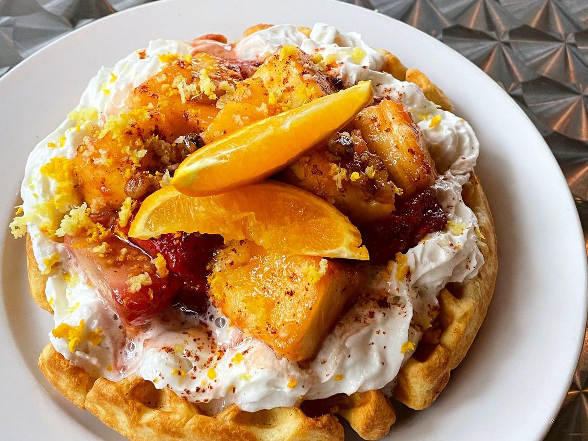 A waffle topped with cooked fruit, whipped cream, slices of oranges, and zest. 
