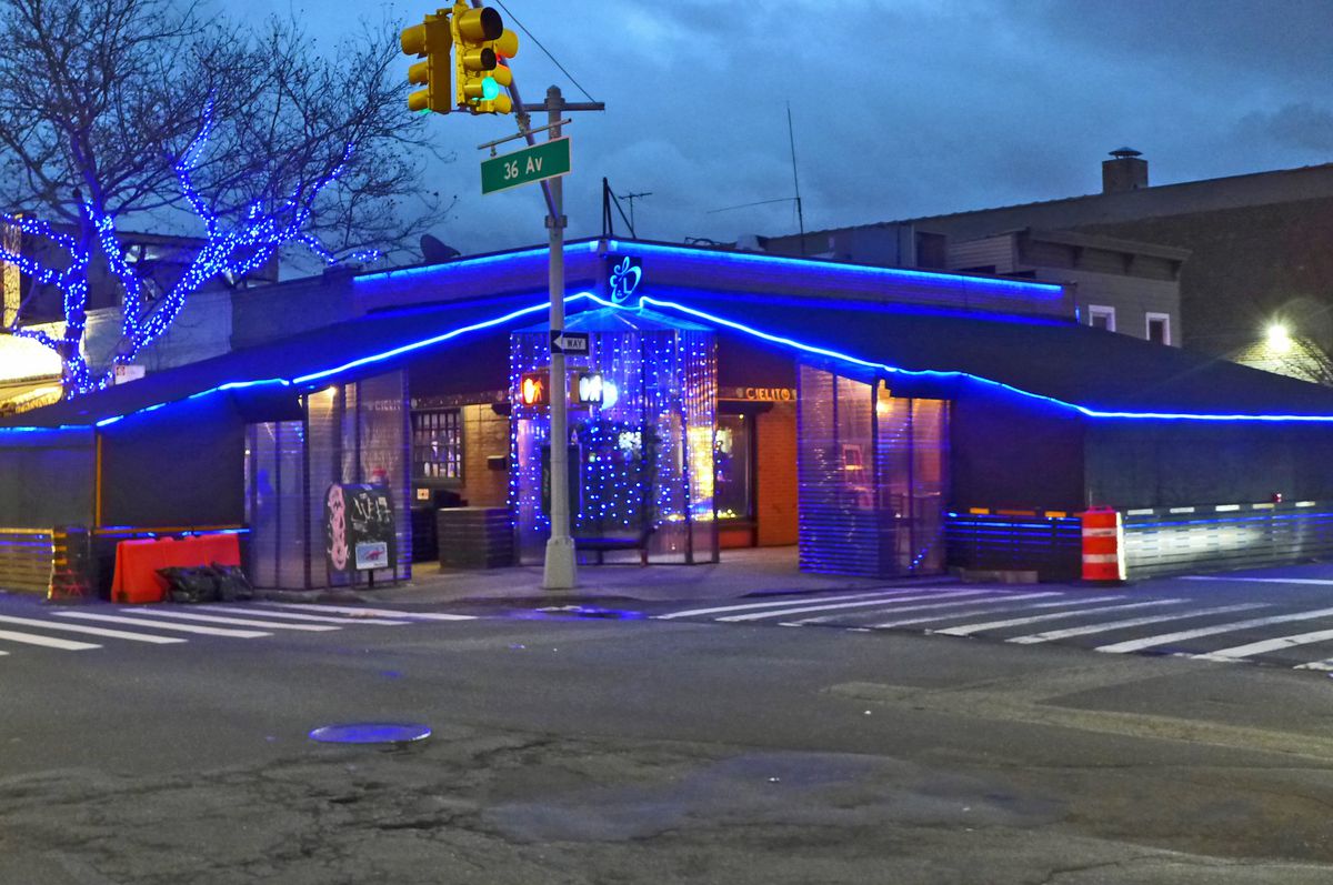 A ranch style corner bar glows blue in the twilight sky.