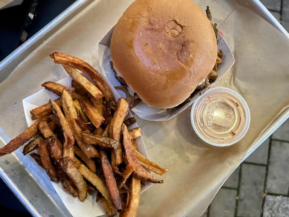 A tray with a vegetarian pulled pork sandwich, fries, and a side cup of sauce.