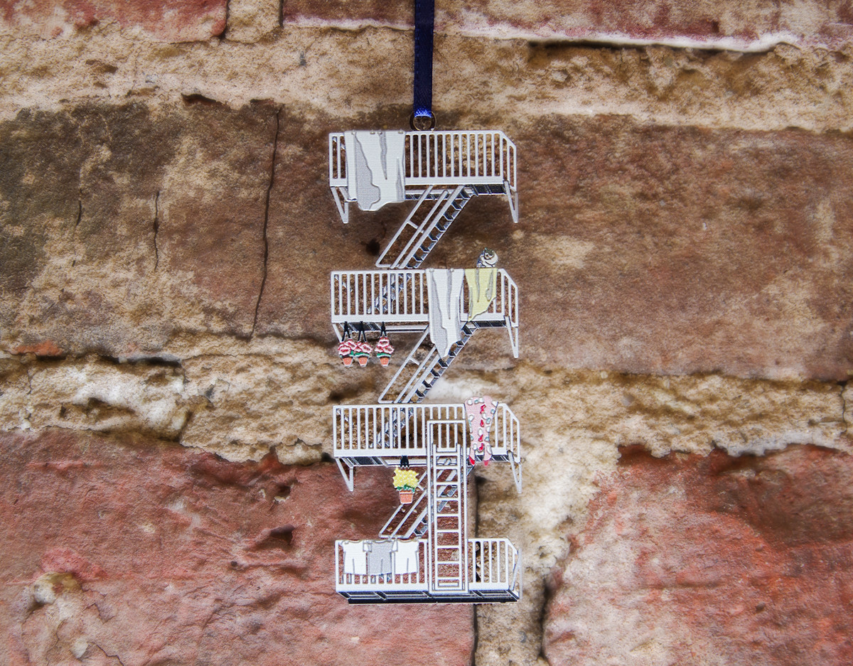 An ornament shaped like a New York City fire escape is hanging in front of a red brick background.