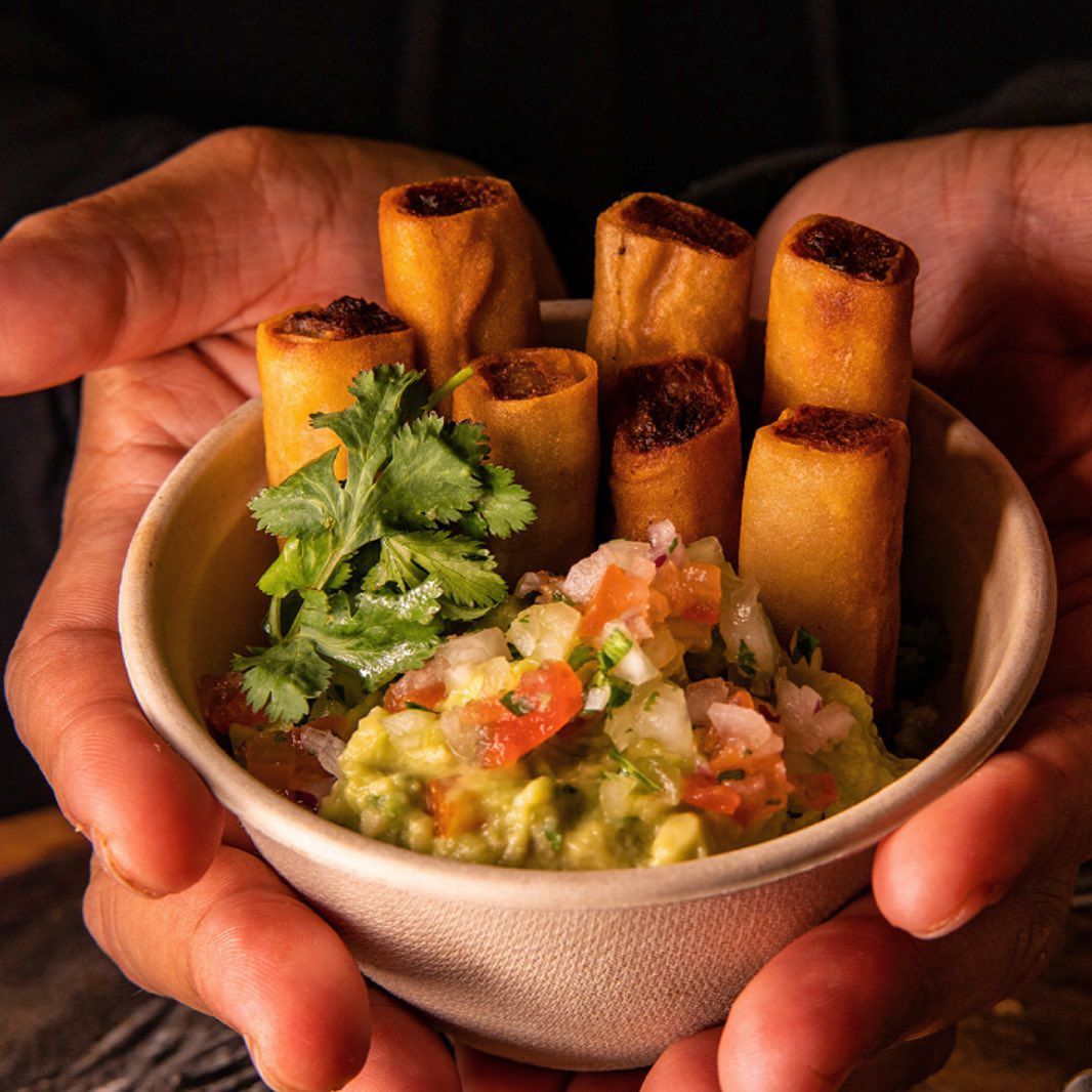 Hands cradle a bowl of lumpia Shanghai and guacamole inspired by the chips and guacamole from NYC Filipino pop-up So Sarap. 