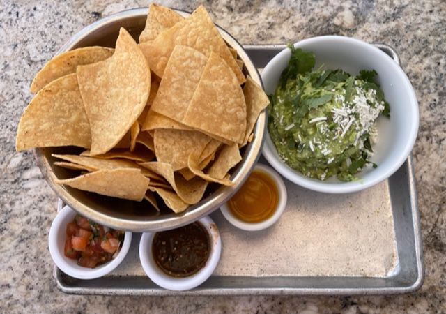 A metal tray shown from above with dishes of guacamole, chips, and three salsas.