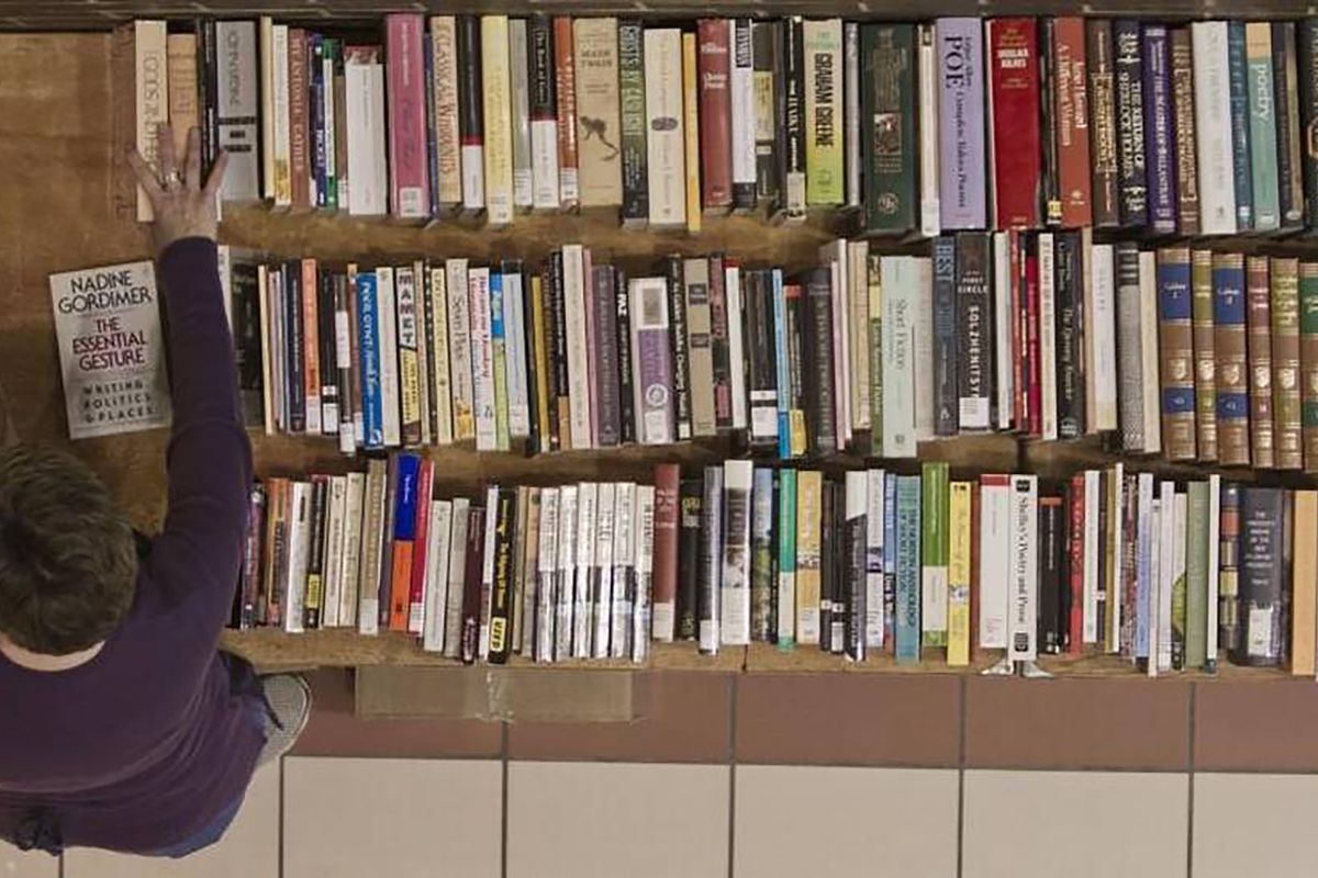 A person holds a book in their hand while looking down at a long table full of books, shown from above.