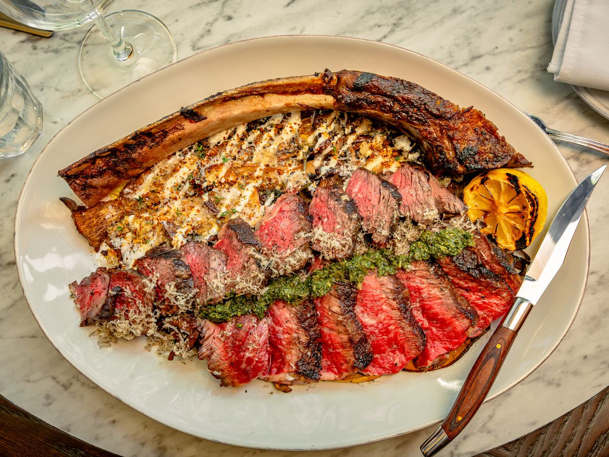 A large steak sliced up and arranged on an oval white plate, with a steak knife balanced on the side of the dish.