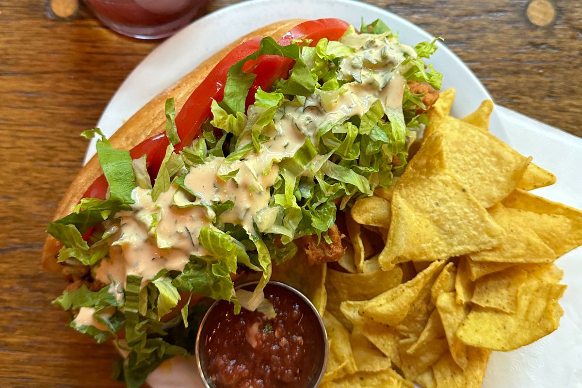 A photo of the buffalo soy curl sub with a side of chips and salsa and a cocktail at the Sweet Hereafter vegan bar.