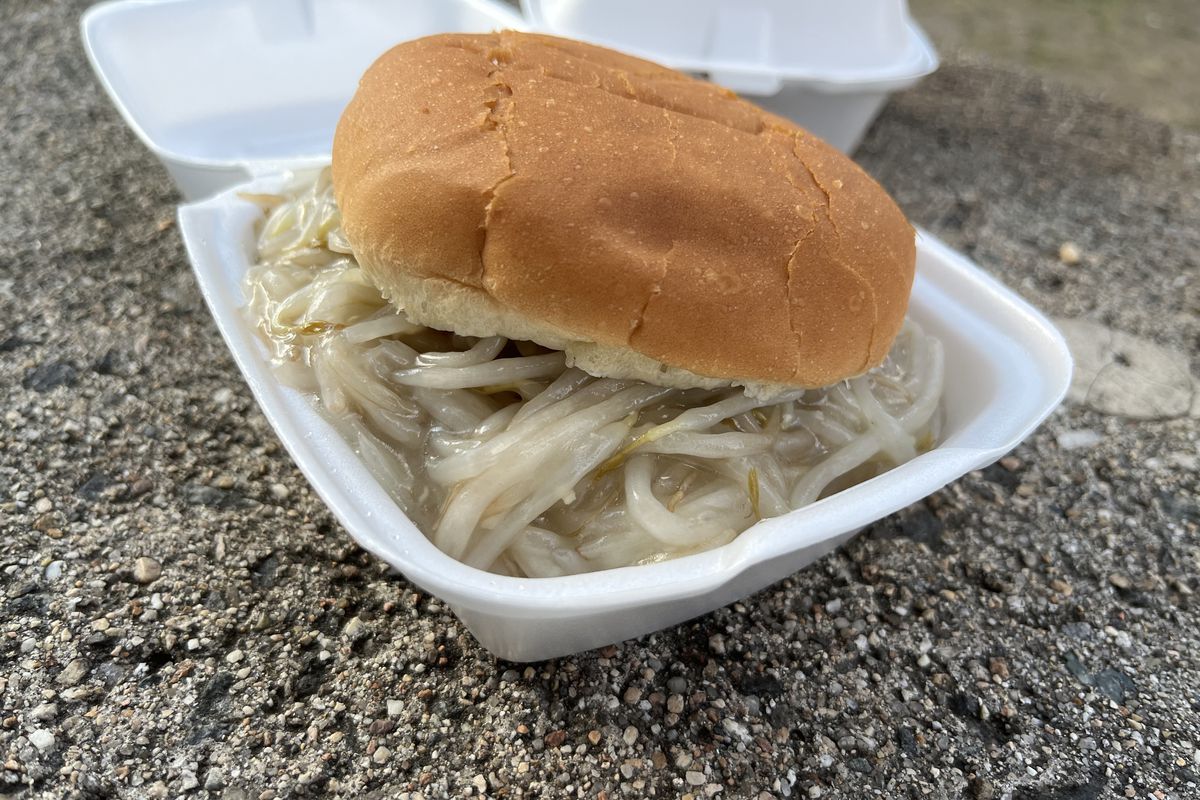 A pile of bean sprouts in a cornstarchy gravy sits on a hamburger bun in a small white styrofoam container.