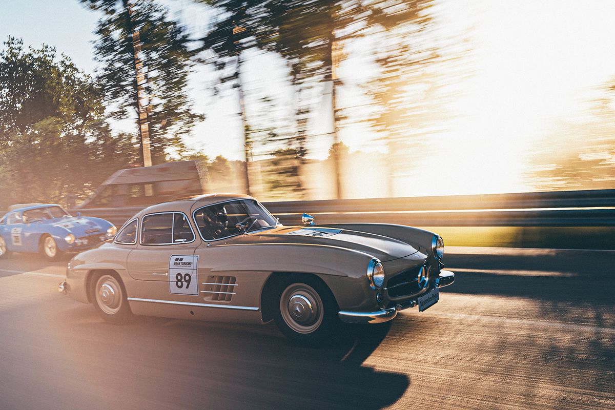 Classic Mercedes sports cars race past a setting sun