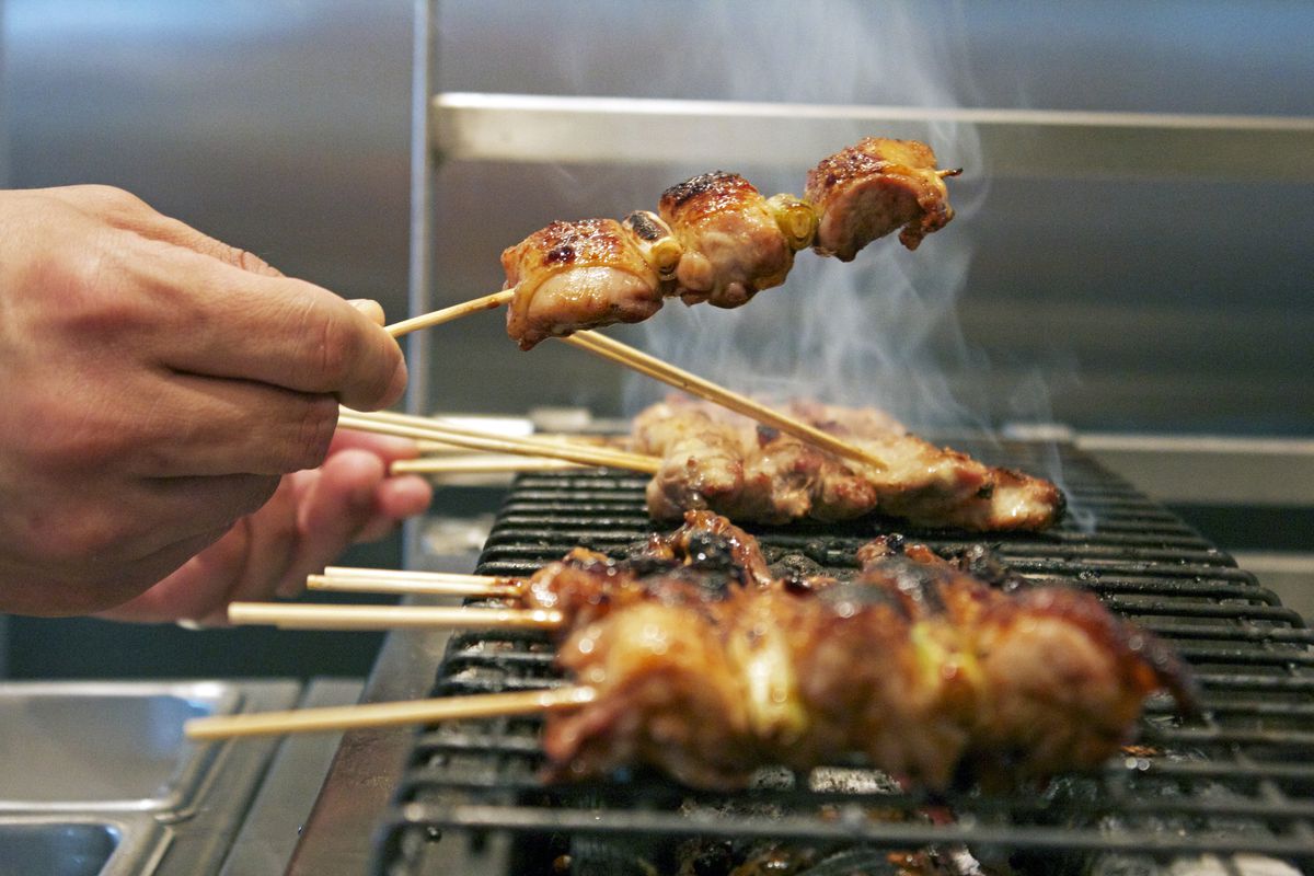 A hand holds skewers aloft a grill at Pabu in Boston