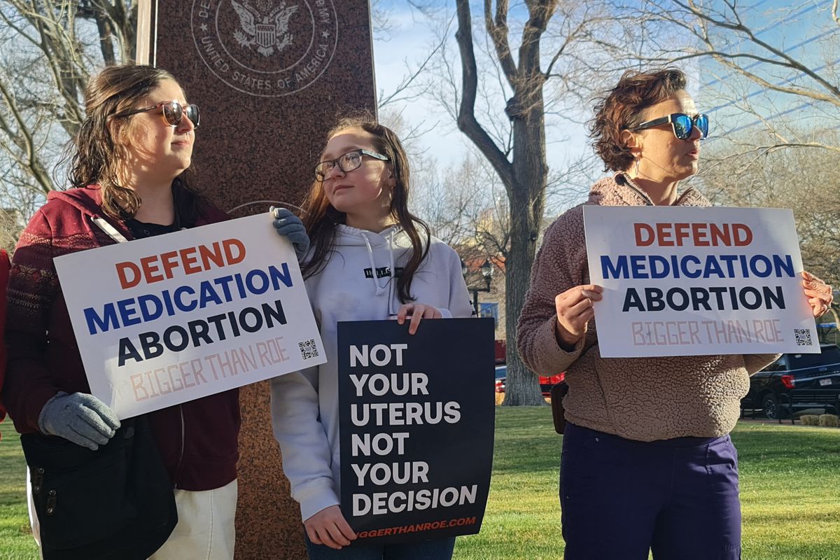 Three people stand holding signs that read, “Defend medication abortion,” and “Not your uterus, not your decision.”