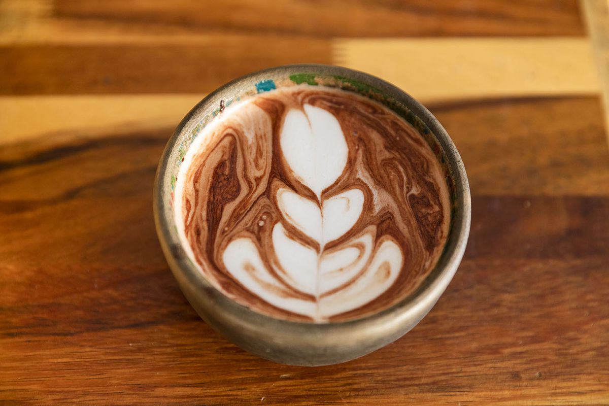 Latte-like art tops a chocolate drink in a clay cup.