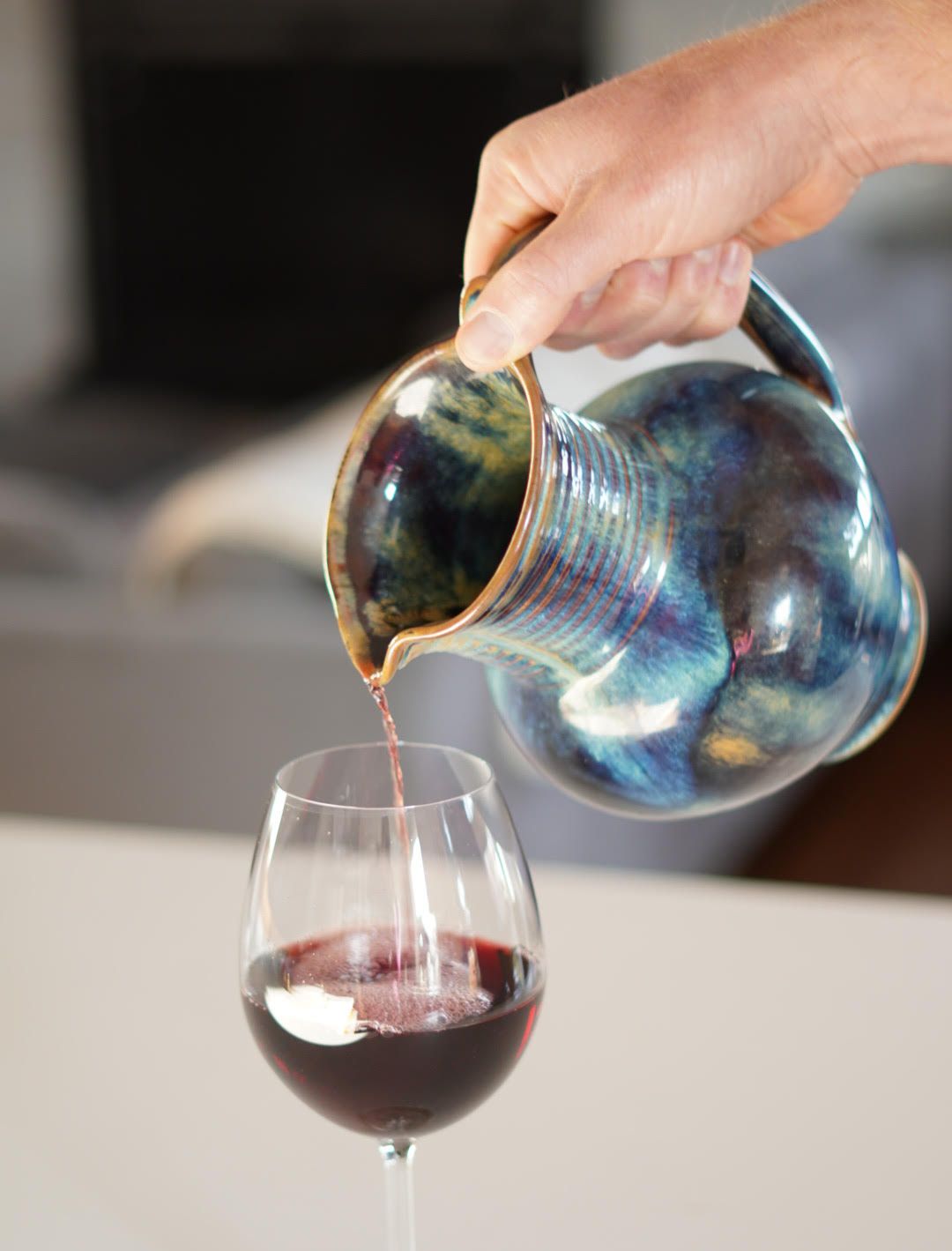 A blue handmade wine pitcher pours wine into a mostly full crystal glass.