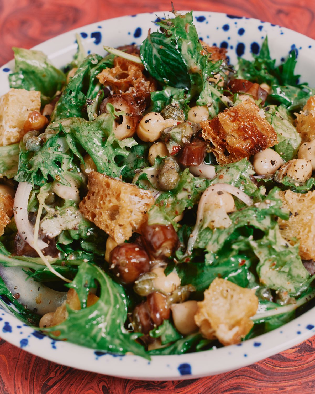 A close-up photo of a well-dressed green salad with croutons and chickpeas visible.