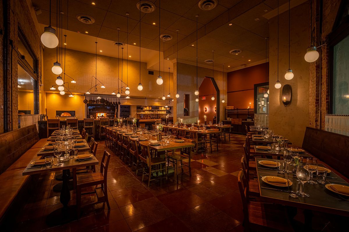 A golden restaurant at night showing communal wooden tables and a long open kitchen.
