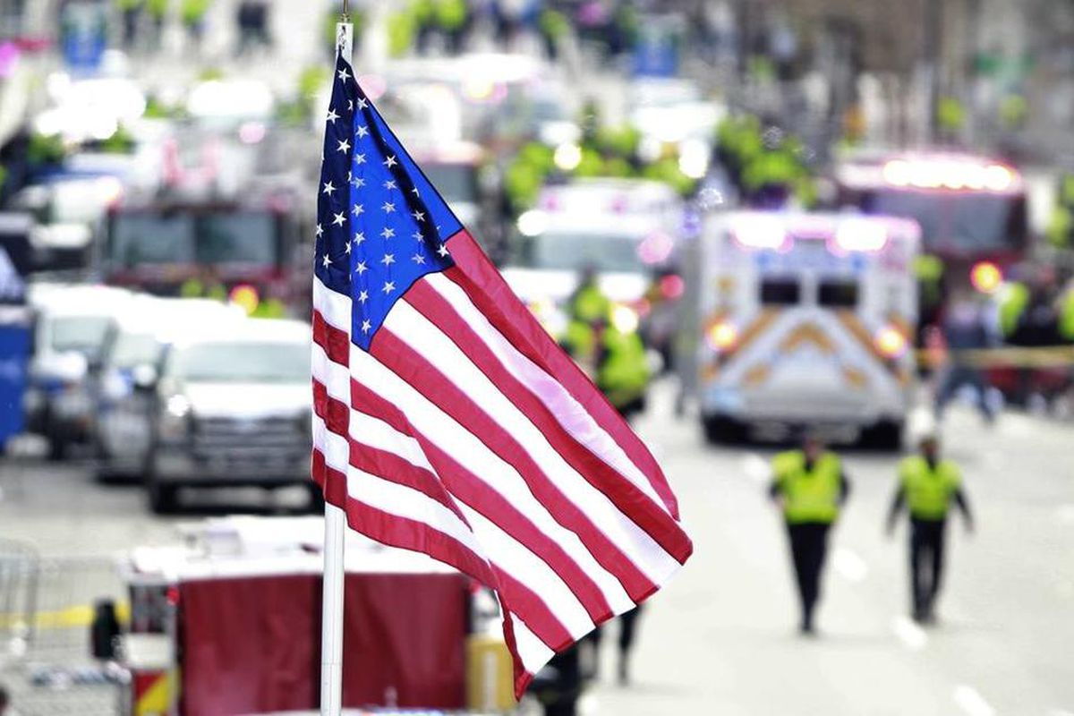 A flag flies over the finish line as medical workers aid injured people following an explosion at the finish line of the 2013 Boston Marathon in Boston, Monday, April 15, 2013. Two explosions shattered the euphoria at the finish line, sending authorities 