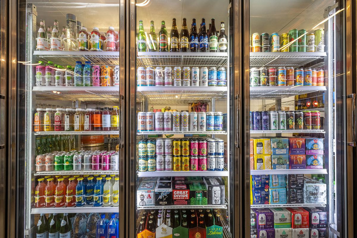 Whole rows of drinks inside of a beverage cold case with clear glass doors.