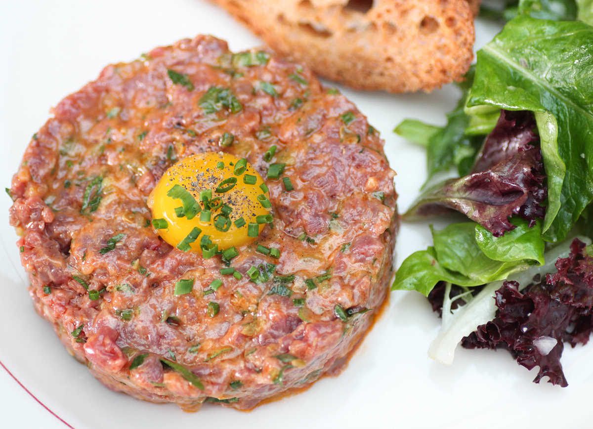 Steak tartare with an egg yolk on top and with salad on the side