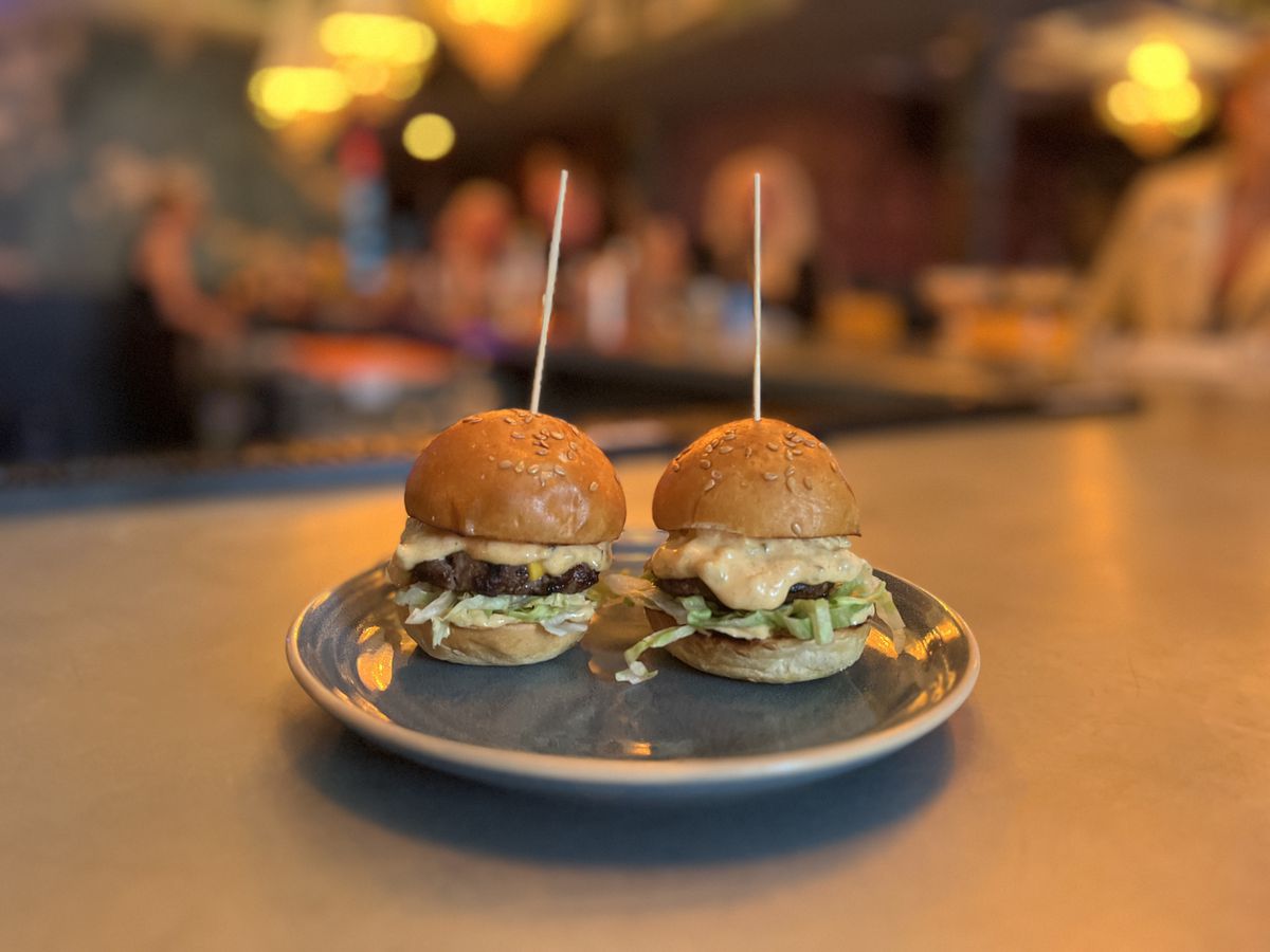Two small burger sliders on a plate with toothpicks sticking out of the top buns.