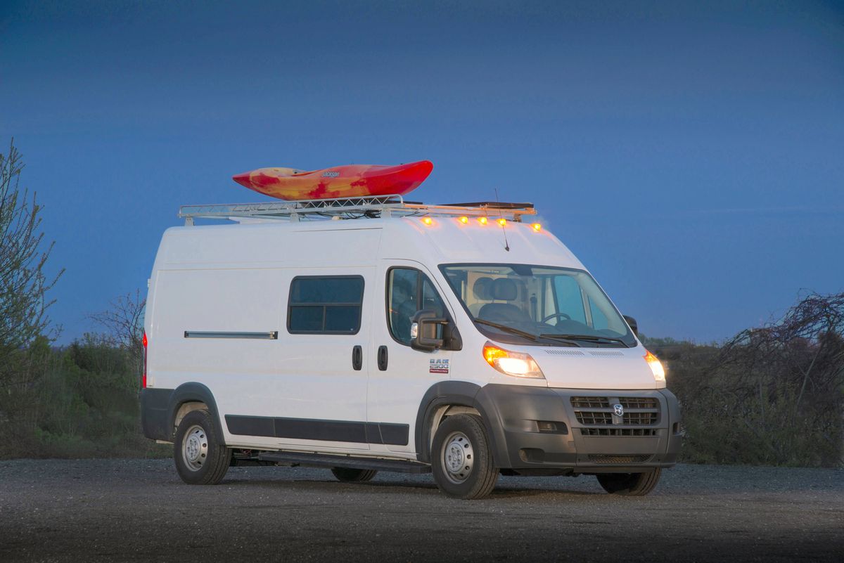 A white van with a roof attachment that has a red boat on it.