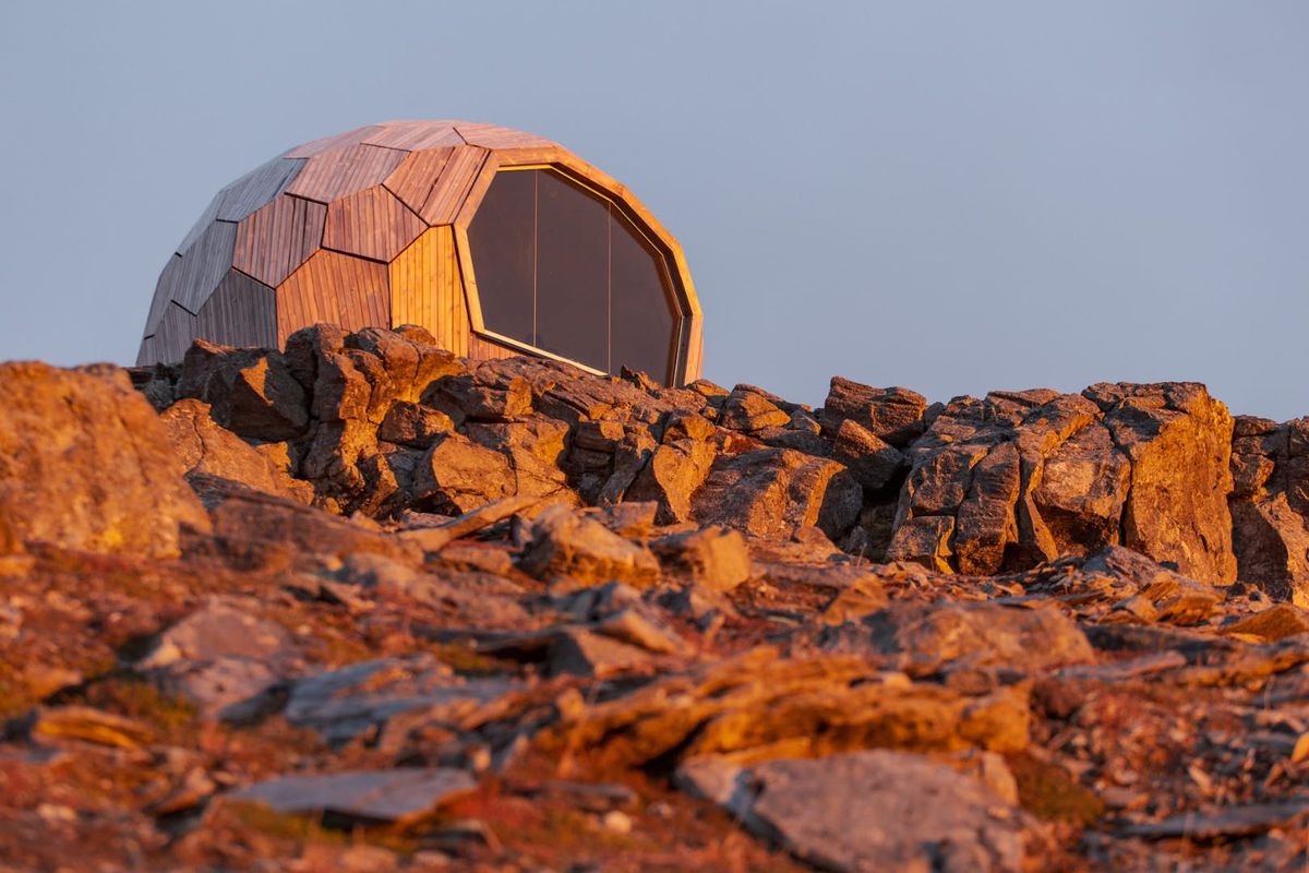 A cabin with a geometric shape is on a mountaintop. 