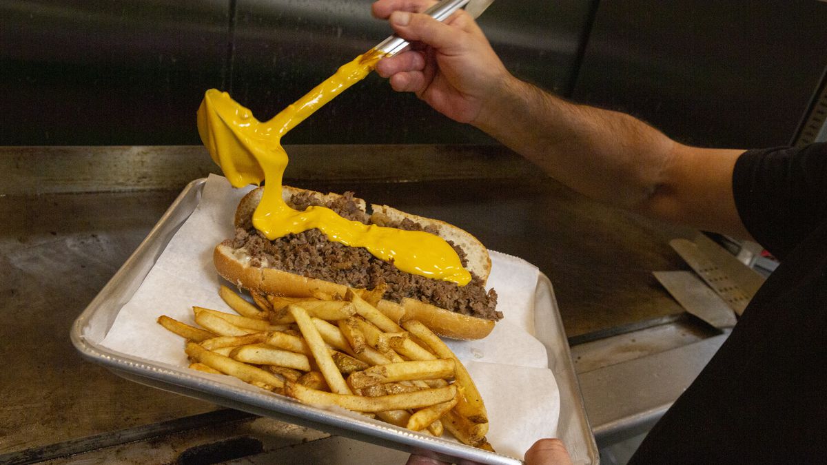 A ladle of Cheez Whiz drops liquid gold onto a beef sandwich.