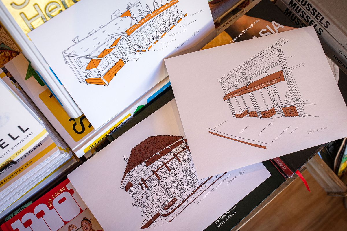 Three drawings of Napa-based restaurant storefronts are displayed inside a bookstore; the restaurants are Mustards, French Laundry, and the Model Bakery.
