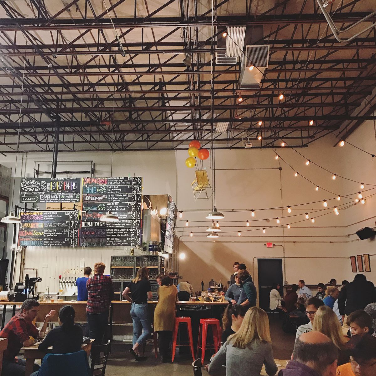 Towering ceilings accommodate a chalkboard beer list, a bar, and table seating inside a brewery