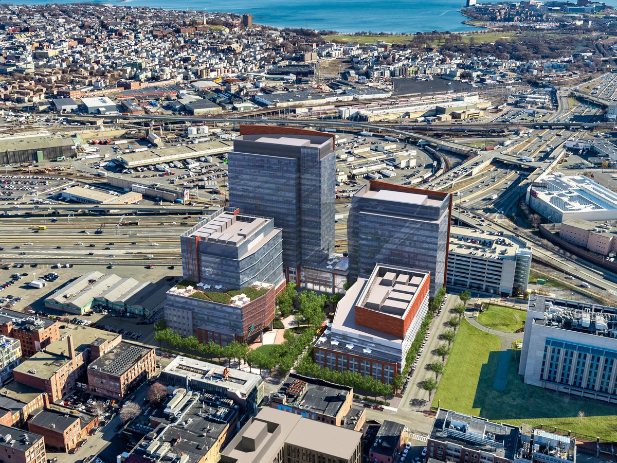 An aerial view of four new buildings amid an urban landscape that includes highways and a harbor.