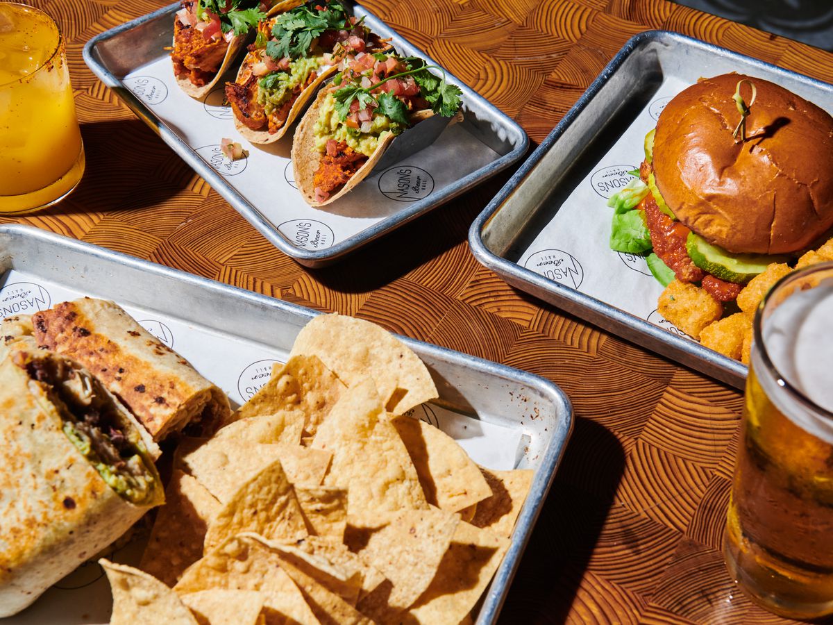 Tacos, a burger, burrito, and beer on a table.
