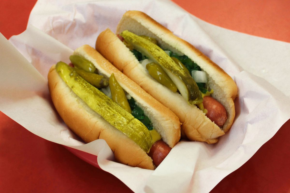 Two Chicago-style hot dogs on a parchment paper in a basket.