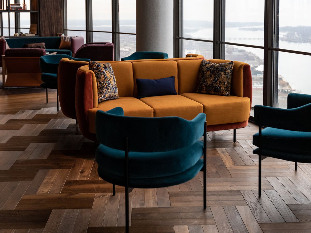 Jewel-toned velvet chairs and sofas on patterned wood floors in the lounge next to windows looking out towards St. Clair Shores.