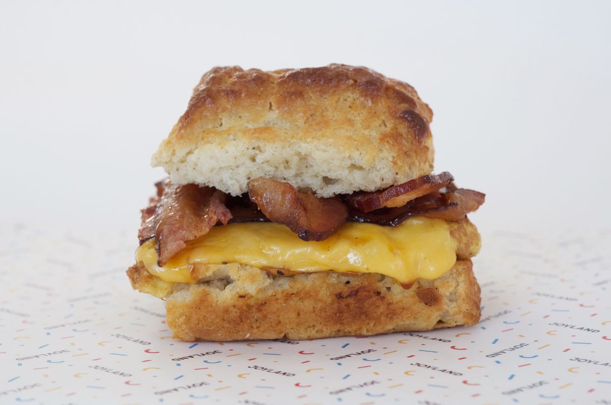 bacon, egg, and cheese biscuit in center of photo, close up, on Joyland printed paper