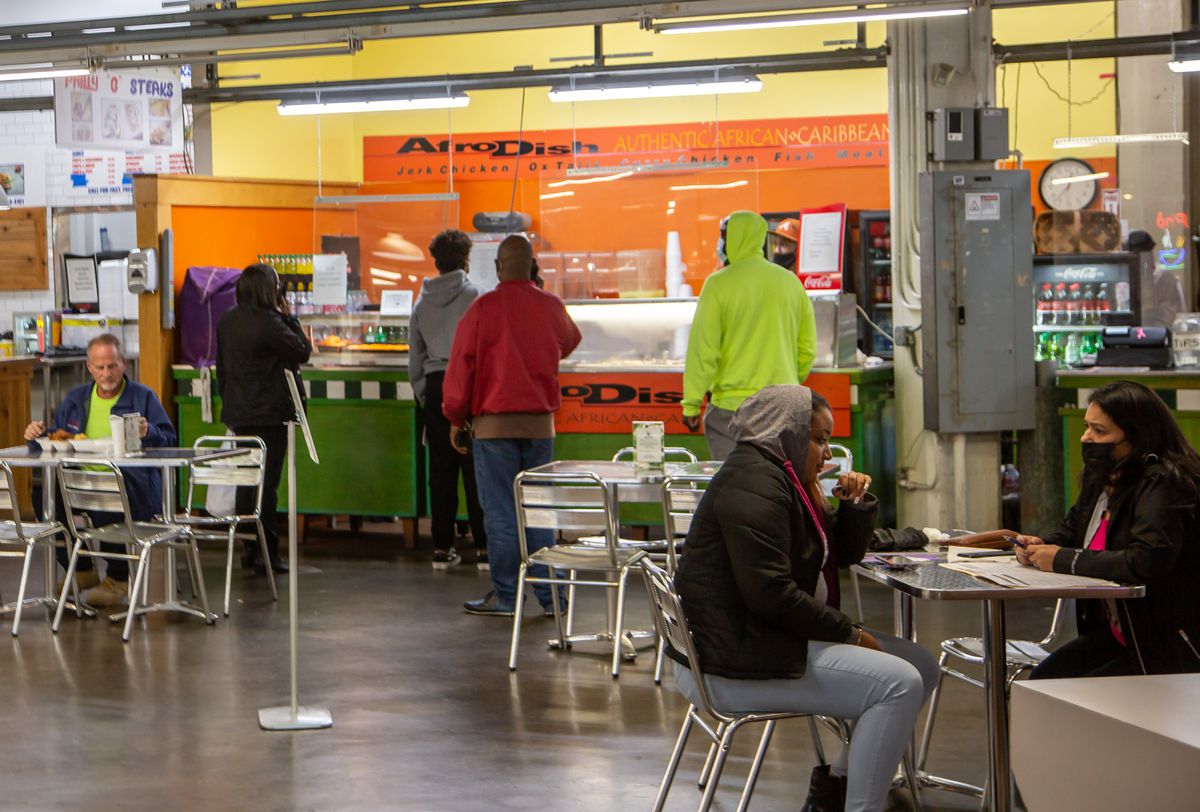 People order food from AfroDish Restaurant stall during lunch inside The Municipal Market of Atlanta, the Sweet Auburn Curb Market, as people sit at tables beyond eating.